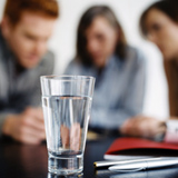 Varios miembros de una empresa reunidos entorno a una mesa con documentación sobre ella y un vaso lleno.