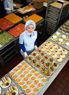 Vista desde arriba, entre dos mesas largas una cocinera muestra diferentes tipos de de platos de gran colorido.