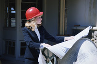 Arquitecta con casco rojo, a pie de obra revisando los planos de una construcción.