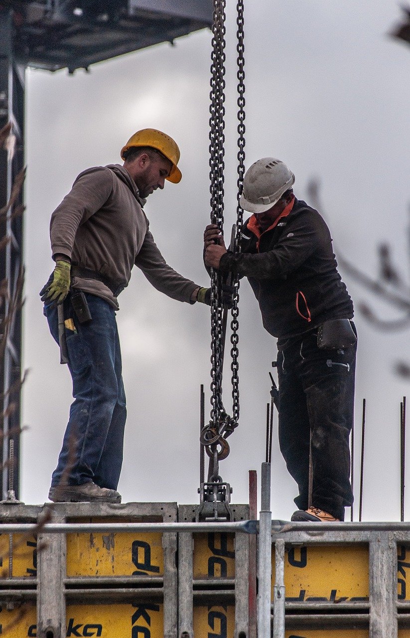 Imagen de dos trabajadores en la obra de un edificio en construcción llevando equipos de protección individual y cumplimiento con sus obligaciones en materia de prevención.