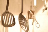 Colección de diversos objetos de cocina, se puede observar en primer plano: dos espumaderas, una tijera y un abrelatas, en segundo plano podemos ver un sacacorchos.