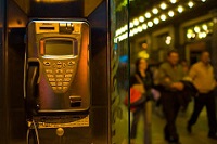 Cabina de teléfonos en rimer plano, con gente al fondo caminando.
