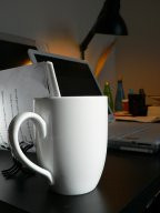 Mesa de trabajo con un ordenador al fondo y una taza en primer plano.